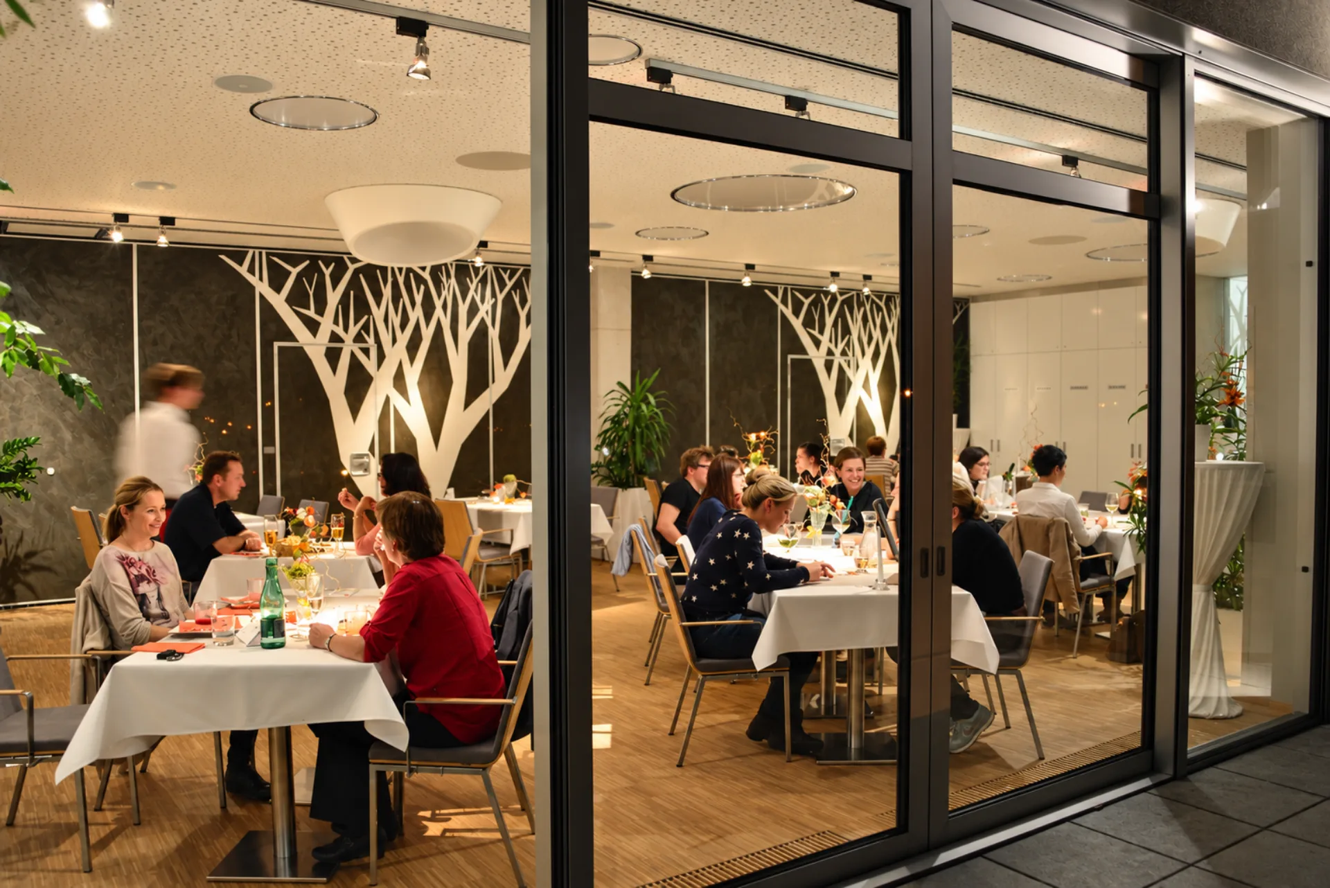 Hosté při večeři v restauraci Hotelu Antonie ve Frýdlantu, pohled přes prosklenou stěnu.